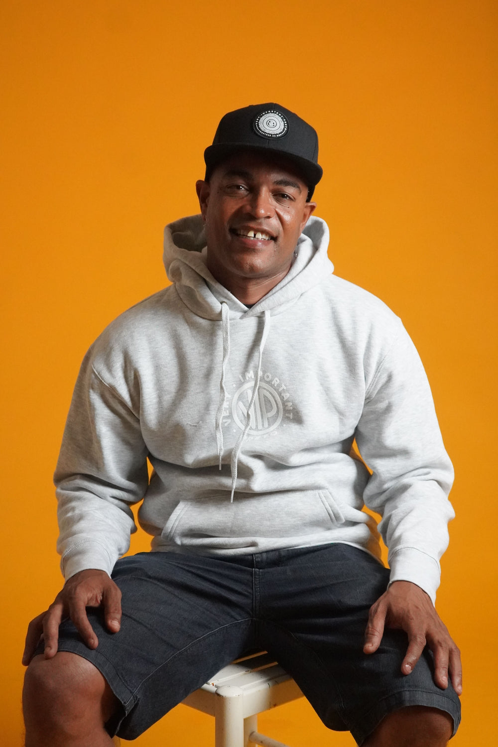 Man wearing a white hoodie and black cap against an orange background